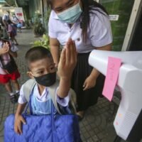 Ein Junge hebt seine Hand für eine Temperaturkontrolle, bevor er seine Schule an der Wat Nong Khaem School in Bangkok betritt.