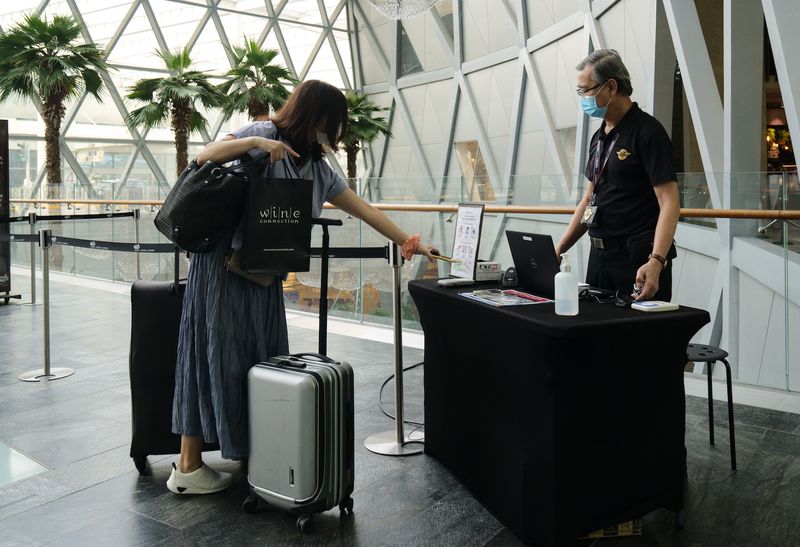 Eine Frau mit einem Koffer benutzt die Trace Together App auf ihrem Handy an einem Scanpunkt, um am 3. Oktober das Einkaufszentrum Jewel Changi Airport in Singapur zu betreten. (Bloomberg Photo)