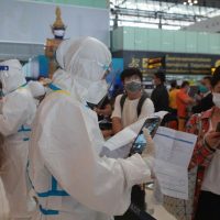 Touristen lassen ihre Dokumente von Arbeitern in PSA Anzügen am Flughafen Suvarnabhumi überprüfen, da die Entdeckung der Omicron Variante in Thailand bei den Betreibern Bedenken auslöste