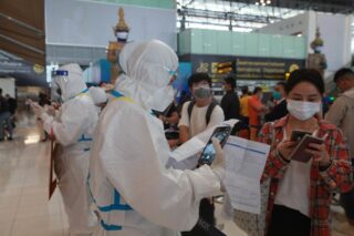 Touristen lassen ihre Dokumente von Arbeitern in PSA Anzügen am Flughafen Suvarnabhumi überprüfen, da die Entdeckung der Omicron Variante in Thailand bei den Betreibern Bedenken auslöste