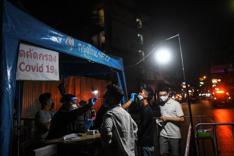 Gesundheitspersonal entnimmt den Menschen Abstrichproben für Antigen Schnelltests, bevor sie am Freitag die Khao San Road, einen der beliebtesten Touristenorte in Bangkok, betreten