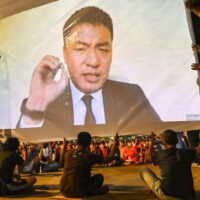 Demonstranten beobachten, wie im März letzten Jahres in Yangon ein Video, das den Sprecher der Schattenregierung, Dr. Sasa, zeigt, auf eine Leinwand projiziert wird. Ihm und mehreren anderen Schlüsselfiguren der Regierung der Nationalen Einheit wurde die burmesische Staatsbürgerschaft aberkannt