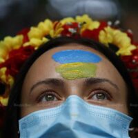 Eine Frau mit den Farben der ukrainischen Nationalflagge auf der Stirn steht vor Demonstranten, die sich am Montag vor der russischen Botschaft in Bangkok versammelt hatten