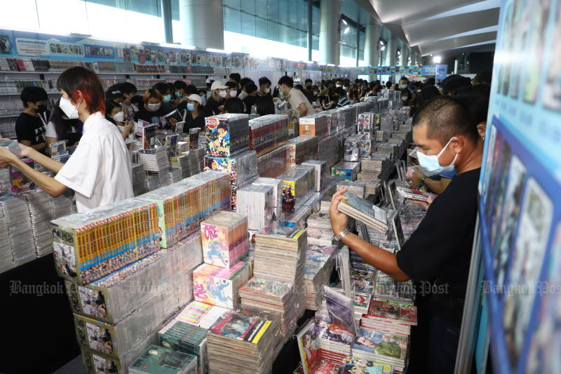 Menschen, die aufgrund des Ausbruchs von Covid-19 Gesichtsmasken tragen, sichten einen Stapel Bücher, während sie auf der 50. Thailand Book Fair nach ihrer Lieblingslektüre suchen.