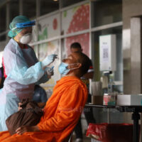 Ein Gesundheitshelfer führt am Donnerstag an einem Busbahnhof in Bangkok einen Abstrich-Antigentest bei einem Mönch durch