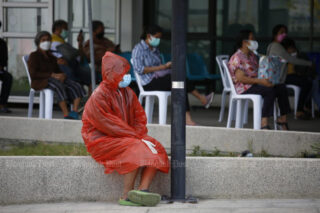 Eine Frau trägt einen Regenmantel, eine Gesichtsmaske und Handschuhe, während sie darauf wartet, dass sie am Sonntag im Bang Khunthian Geriatric Hospital einem ATK-Test auf Covid-19 unterzogen wird