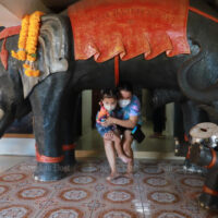 Eine Mutter nimmt ihr Kind am Samstag während eines Besuchs im Wat Sakhla im Distrikt Phra Samut Chedi auf Samut Prakan unter den Bauch einer Elefantenstatue.