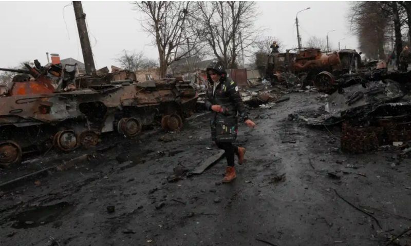 Eine Ukrainerin geht in Bucha an zerstörten russischen Militärfahrzeugen vorbei