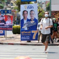 Fußgänger gehen auf der Burapha Road in Bangkok an Wahlkampfplakaten des Gouverneurs vorbei.