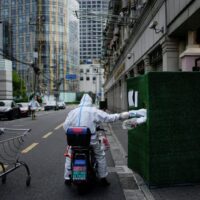 Ein Arbeiter in einem Schutzanzug reicht am Donnerstag Lebensmittel durch eine Lücke in der Barriere in einem Wohngebiet in Shanghai.