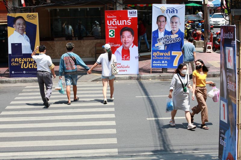 Fußgänger überqueren die Burapha Road, während Wahlkampfplakate des Gouverneurs von Bangkok und des Rates den Straßenrand säumen