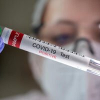 In diesem Illustrationsbild ist ein Reagenzglas mit der Aufschrift „Covid-19-Test positiv“ zu sehen