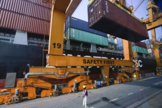 Versandcontainer werden im Hafen von Bangkok auf einen internationalen Frachter verladen. Die Baht-Abwertung macht thailändische Exporte billiger, importierte Rohstoffe werden jedoch teurer