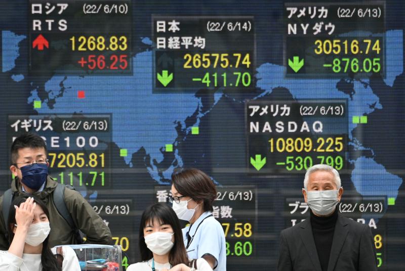 Fußgänger stehen am 14. Juni 2022 in Tokio vor einer elektronischen Kurstafel, auf der die Zahlen des weltweiten Aktienmarktes angezeigt werden, einschließlich der Aktienkurse der Tokioter Börse