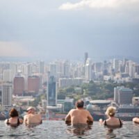Hotelgäste im Infinity-Pool im SkyPark auf dem Marina Bay Sands blicken auf die Skyline der Stadt Singapur.