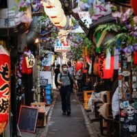 Menschen gehen am 6. Juli in Tokio eine Straße voller Izakaya Kneipen entlang