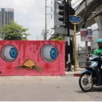 Ein Essensfahrer passiert ein neues Graffiti mit dem Titel „Farmer’s Tears 2022“, das am 16. April 2022 in der Soi Sukhumvit 74, von einem bekannten Mue-Bon-Künstler gemalt wurde.