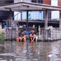 Jungen unterhalten sich, während sie mit ihren Füßen im Hochwasser in der Gemeinde Wat In in Nonthaburi sitzen,