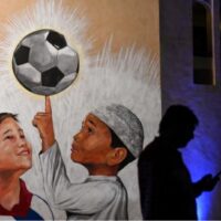 Ein Mann benutzt sein Handy am Freitag vor dem Fußballturnier der FIFA Fussball-Weltmeisterschaft Katar 2022 neben einem Wandbild in Doha.